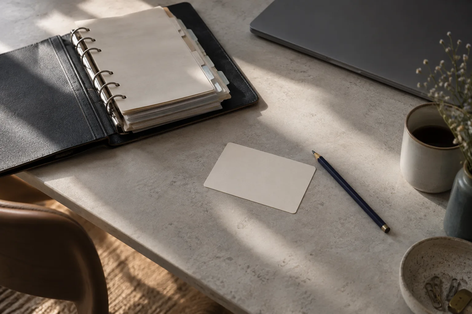 A single blank card and indigo pencil beside a thick organizer and closed laptop.